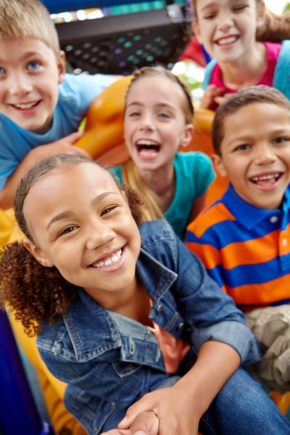 A happy group of multi-ethnic children sitting happily on a slide in a play park.